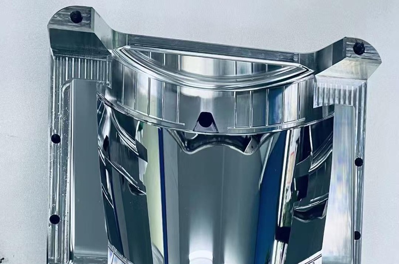 Mirror-finished automotive reflector mold core with curved surfaces and detailed optical transitions.
