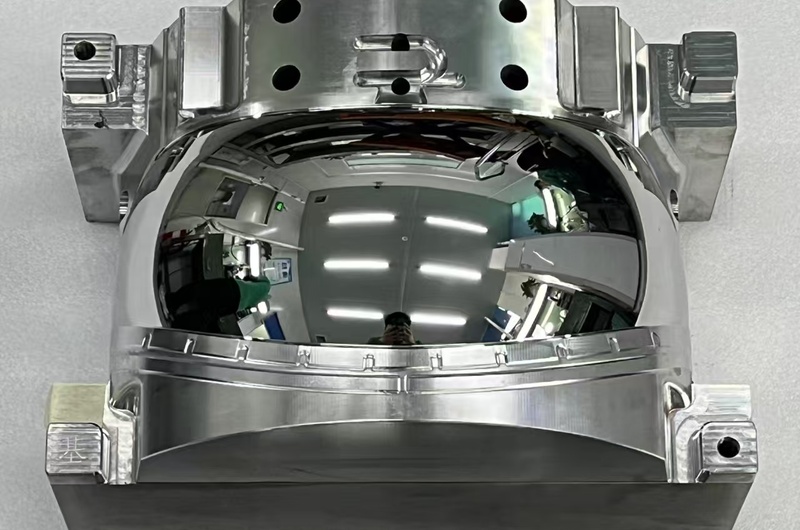 Custom mirror-polished automotive reflector mold insert with a deep curved optical cavity.